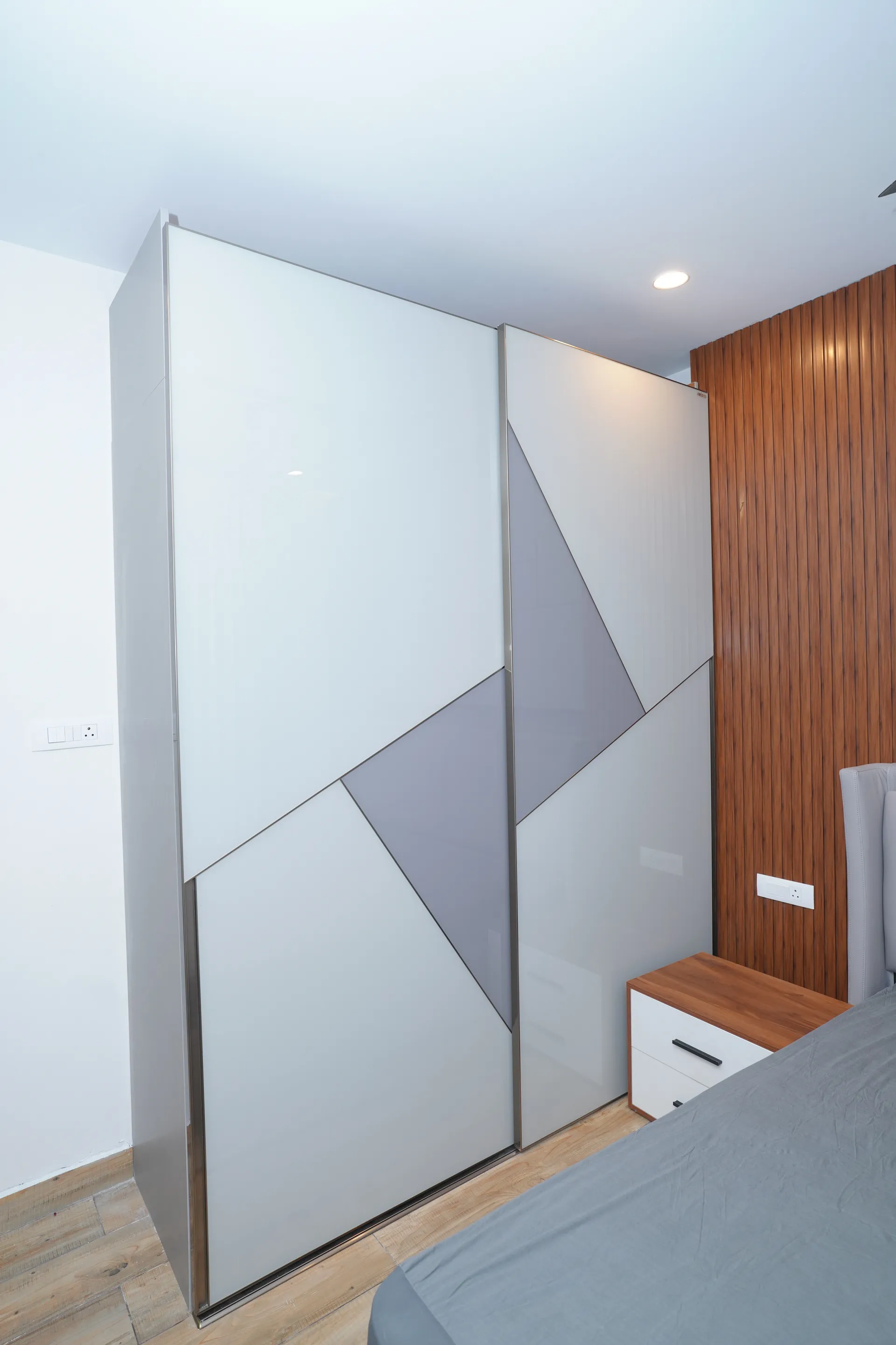 Sliding wardrobe with white and grey geometric glossy shutters beside a walnut fluted panel, villa at SVS Silver Oaks, Heelalige